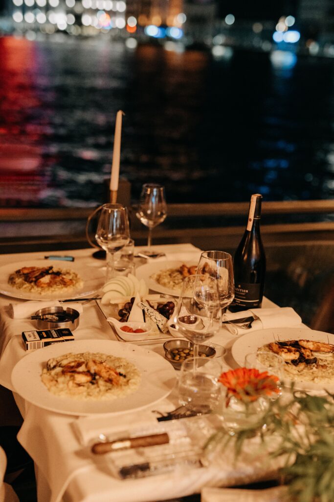 Elegant waterfront dinner scene with candlelit table setting, featuring gourmet meal and wine.