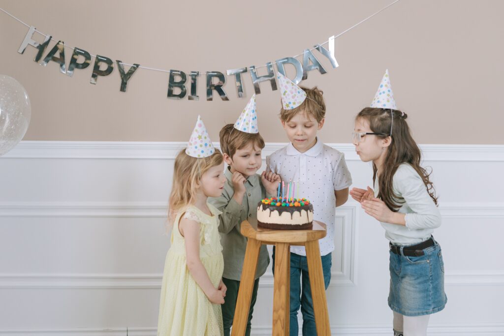 Group of children celebrating a birthday with cake and decorations indoors.