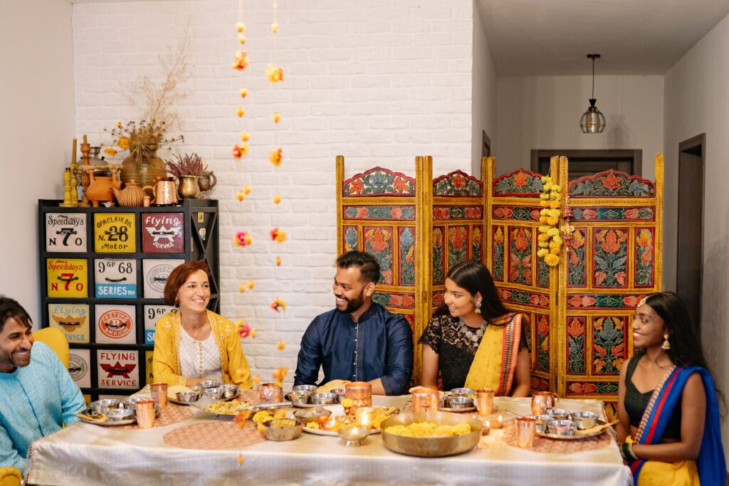 A joyful Indian family celebration with traditional clothing and festive foods, gathered around a dinner table.